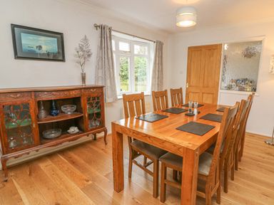 A dining room with a wooden table and chairs a sideboard with glass shelves a window with curtains and a wooden door at Trederwen in Rhayader