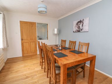 A dining room with a wooden table and six chairs a painting of a horse on the wall and a wooden door at Trederwen in Rhayader