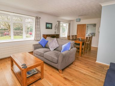 A living room with a gray couch and blue pillows a wooden coffee table and dining table with chairs at Trederwen in Rhayader