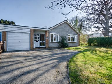 A front view of a house with a garage and driveway and a lawn with trees at Trederwen in Rhayader