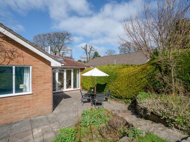 A patio with outdoor table umbrella and chairs next to a brick house and garden at Trederwen in Rhayader