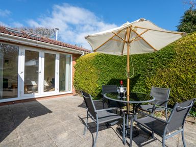 An outdoor patio area with a round glass table four chairs and a large umbrella next to a building with glass doors at Trederwen in Rhayader