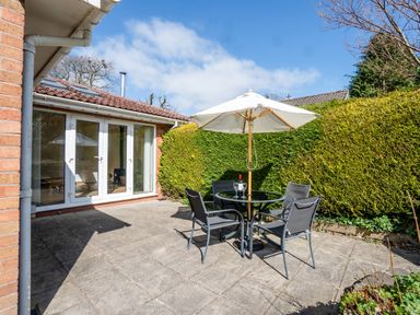 A patio with a round table four chairs and a large umbrella next to a hedge at Trederwen in Rhayader