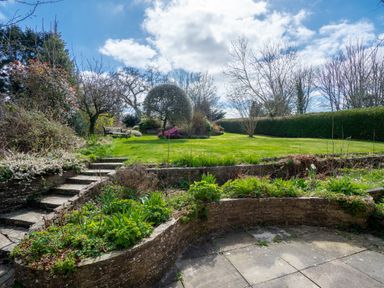 A garden with stone steps leading to a lawn with trees and a bench at Trederwen in Rhayader