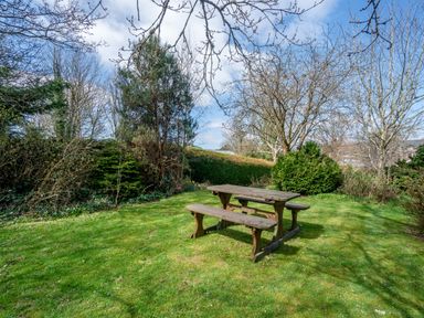 A wooden picnic table on grass surrounded by trees and bushes in a garden