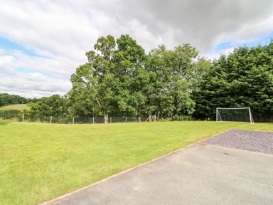 An outdoor grassy area with a soccer goal near trees and a paved surface at Red Kite Cottage in Howey near Llandrindod Wells