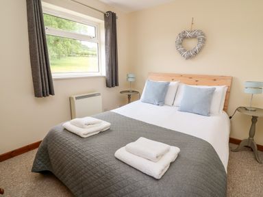 A bedroom with a double bed two bedside tables lamps and a window showing greenery outside at Red Kite Cottage in Howey near Llandrindod Wells