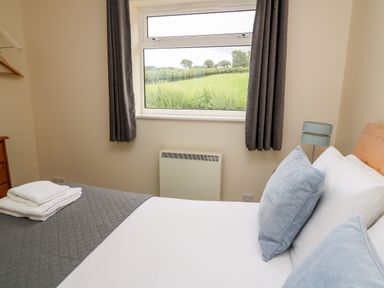 A bedroom with a bed made with white sheets and blue pillows by a window with gray curtains at Red Kite Cottage in Howey near Llandrindod Wells