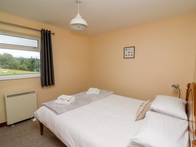 A bedroom with a double bed a window with a curtain a wall heater and a framed picture at Red Kite Cottage in Howey near Llandrindod Wells