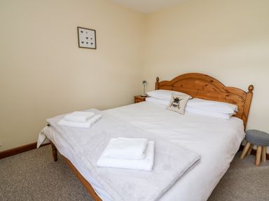 A bedroom with a wooden double bed a bedside table with a lamp white towels on the bed and a small framed picture on the wall at Red Kite Cottage in Howey near Llandrindod Wells