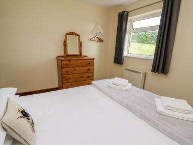 A bedroom with a bed folded towels on a blanket a wooden chest of drawers with a mirror and a window with curtains at Red Kite Cottage in Howey near Llandrindod Wells