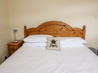 A bedroom with wooden bed headboard white bedding and a bee cushion at Red Kite Cottage in Howey near Llandrindod Wells