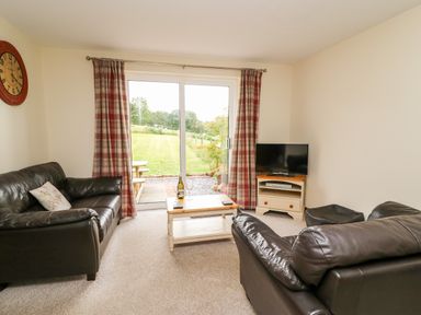 A living room with two leather sofas a wooden coffee table and a television with glass doors overlooking a garden at Red Kite Cottage in Howey near Llandrindod Wells
