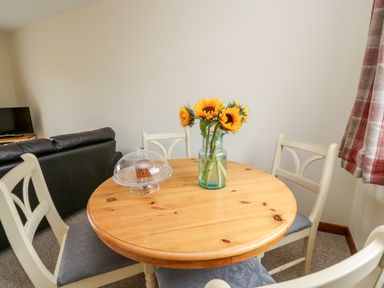 A wooden dining table with four chairs a vase with sunflowers and a cake under a glass dome at Red Kite Cottage in Howey near Llandrindod Wells