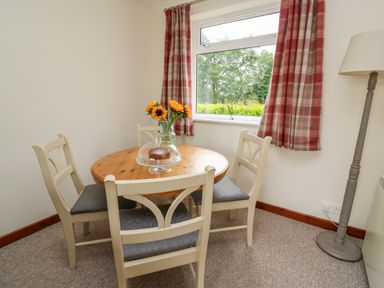 A dining area with a round wooden table surrounded by four cream-colored chairs with grey cushions at Red Kite Cottage in Howey near Llandrindod Wells