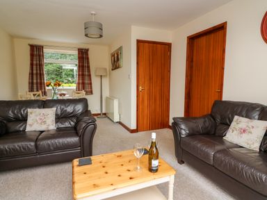 A living room with two leather sofas a wooden coffee table with a bottle and glass two wooden doors and a dining table by a window at Red Kite Cottage in Howey near Llandrindod Wells