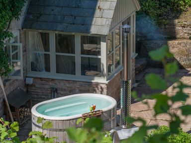 An outdoor hot tub with drinks on the edge near a stone building with windows at Mill Cottage in Hanley William near Tenbury Wells