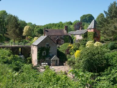 A stone building with attached houses surrounded by trees and greenery at Mill Cottage in Hanley William near Tenbury Wells