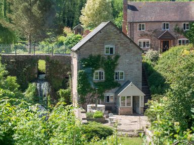A stone house with vines and a water feature with a small waterfall at Mill Cottage Hanley William near Tenbury Wells
