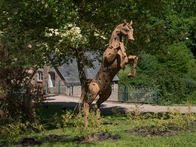 A metal horse sculpture rearing on its hind legs in a garden with trees and a stone building in the background at Mill Cottage in Hanley William near Tenbury Wells