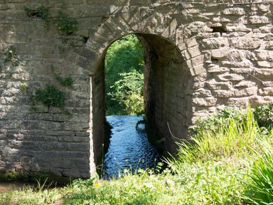 A stone archway with water flowing underneath and green vegetation around at Mill Cottage in Hanley William near Tenbury Wells