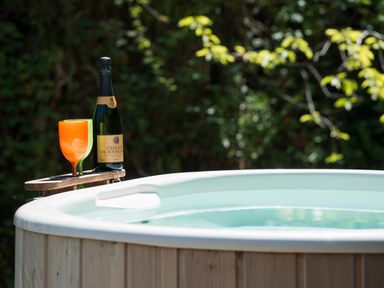 A wooden hot tub with a bottle of sparkling wine and an orange drink on a holder at Mill Cottage in Hanley William near Tenbury Wells