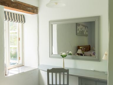 A room with a window a wall mirror a vase with flowers a chair and a desk at Mill Cottage in Hanley William near Tenbury Wells
