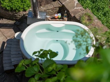 An outdoor hot tub filled with water surrounded by stone walls and greenery at Mill Cottage in Hanley William near Tenbury Wells