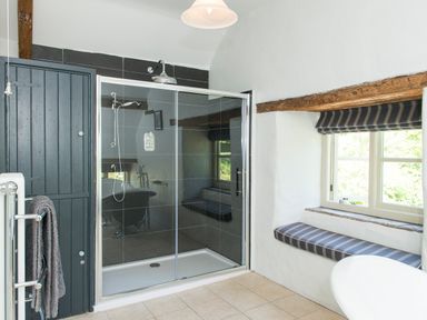 A bathroom with a glass shower enclosure a window seat with cushions and a towel rack at Mill Cottage in Hanley William near Tenbury Wells