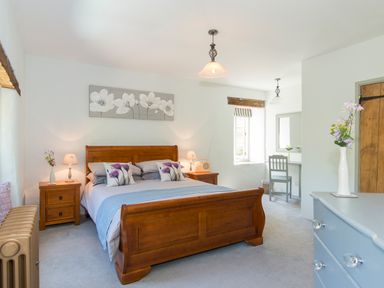 A bedroom with a wooden bed and nightstands a light blue dresser and a small desk with a chair at Mill Cottage in Hanley William near Tenbury Wells