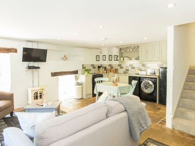 An open plan living area with sofas a coffee table a wall-mounted tv a dining table and kitchen appliances at Mill Cottage in Hanley William near Tenbury Wells