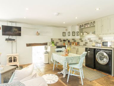 A kitchen and dining area with a table, two chairs, stove, washing machine, microwave and television at Mill Cottage Hanley William near Tenbury Wells