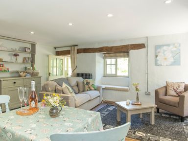A living room with sofas a coffee table and a dining table with flowers and drinks at Mill Cottage in Hanley William near Tenbury Wells