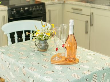A kitchen table with a floral arrangement bottle of sparkling wine and two glasses at Mill Cottage Hanley William near Tenbury Wells