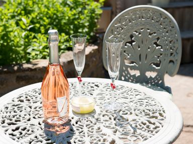 A white ornate metal garden table with a bottle of rose wine two empty champagne flutes and a small candle outdoors