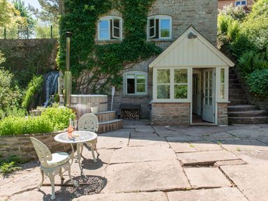 A stone patio with a metal table and chairs in front of a stone building with ivy at Mill Cottage in Hanley William near Tenbury Wells