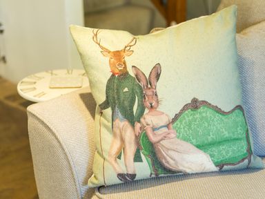 A decorative cushion with a vintage-style illustration of a deer in a suit and a rabbit in a dress on a sofa at Mill Cottage in Hanley William near Tenbury Wells