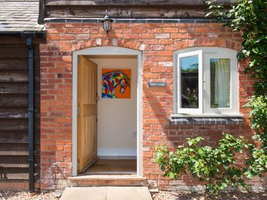 An open wooden door in a brick wall with a colorful horse painting inside at Stable Cottage Hanley William near Tenbury Wells
