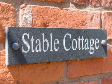 A close up of a black nameplate mounted on a brick wall with the text Stable Cottage