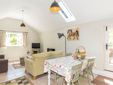 A dining table with chairs and a living area with sofas and a television at Stable Cottage Hanley William near Tenbury Wells
