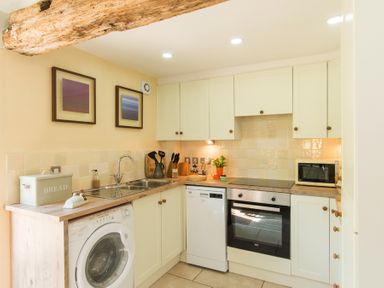 A kitchen with white cabinets a washing machine an oven a dishwasher and a microwave at Stable Cottage in Hanley William near Tenbury Wells