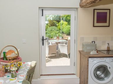 A kitchen area with a washing machine bread box table with flowers and a glass door opening to an outdoor patio at Stable Cottage Hanley William near Tenbury Wells
