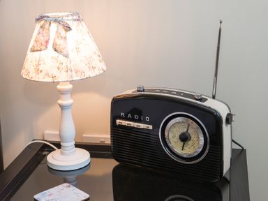 A table lamp with a floral shade next to a vintage radio on a black glass table at Stable Cottage Hanley William near Tenbury Wells