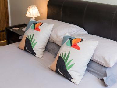 A bed with white and gray sheets and two decorative pillows with colorful toucan designs at Stable Cottage in Hanley William near Tenbury Wells