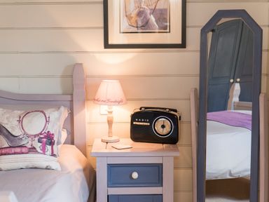 A bedroom corner with a bed a nightstand a lamp a radio and a standing mirror at Stable Cottage Hanley William near Tenbury Wells