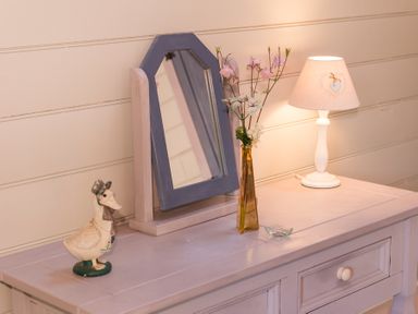 A table with a duck figurine a mirror with a blue frame a vase with flowers and a lamp on it at Stable Cottage in Hanley William near Tenbury Wells