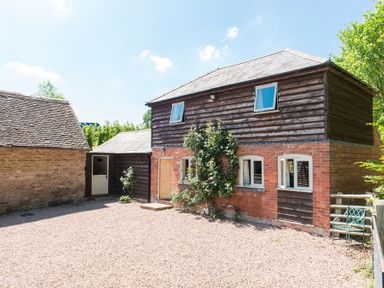 An exterior view of a two-story building with brick and wood siding next to a stone building at Stable Cottage in Hanley William near Tenbury Wells