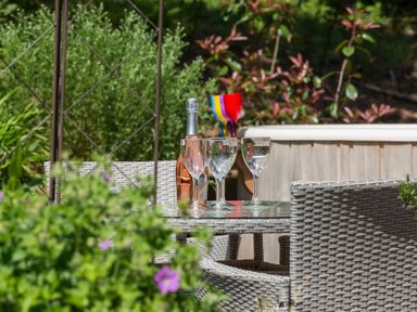 A garden table with a bottle and three glasses surrounded by wicker chairs at Stable Cottage Hanley William near Tenbury Wells