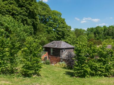 A house surrounded by trees and grass under a blue sky at Stable Cottage Hanley William near Tenbury Wells