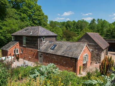 A group of brick and stone buildings surrounded by greenery and trees at Stable Cottage Hanley William near Tenbury Wells